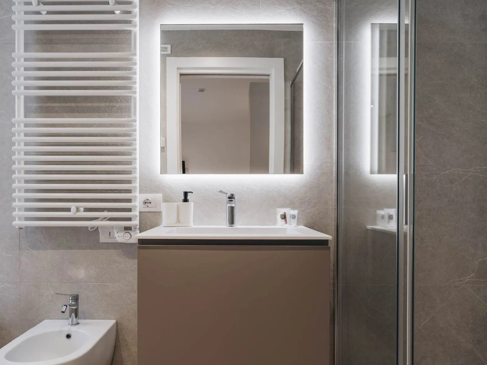 Bathroom with wall-mounted washbasin, backlit mirror, heated towel rail and glass shower enclosure – apartment T-01 Ca' Sette Treviso