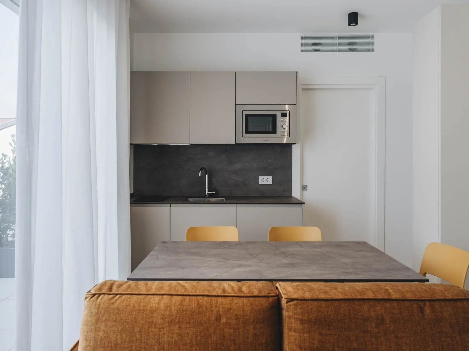 Linear kitchen with taupe wall units, integrated microwave and access to the private terrace – apartment T-01 Ca' Sette Treviso
