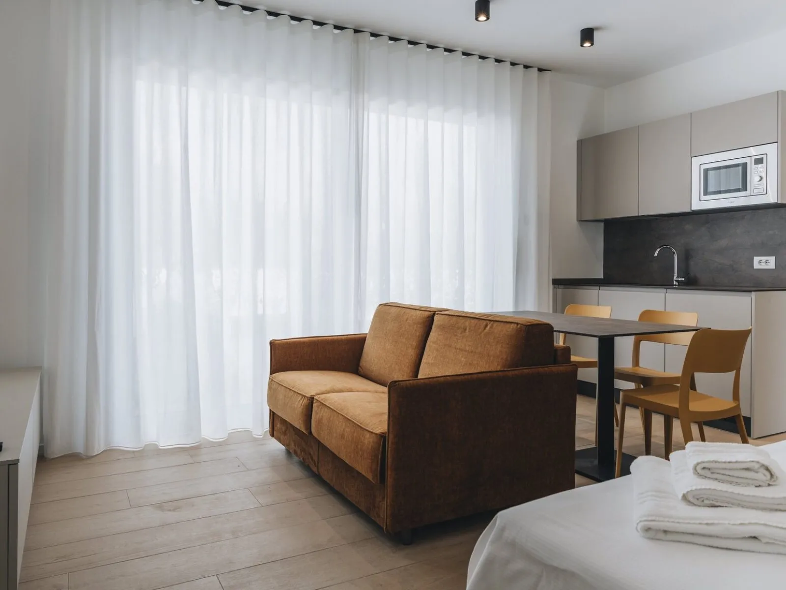Living area with rust-coloured sofa, dining table, mustard chairs and equipped kitchen in the background – apartment T-01 Ca' Sette Treviso