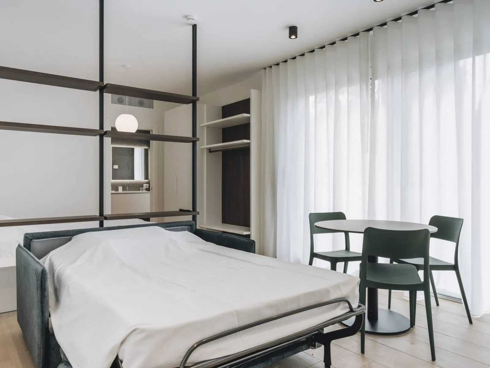 Divano letto aperto nella zona living, con letto matrimoniale e divisorio a scaffale sullo sfondo – appartamento T-05 Ca' Sette Treviso