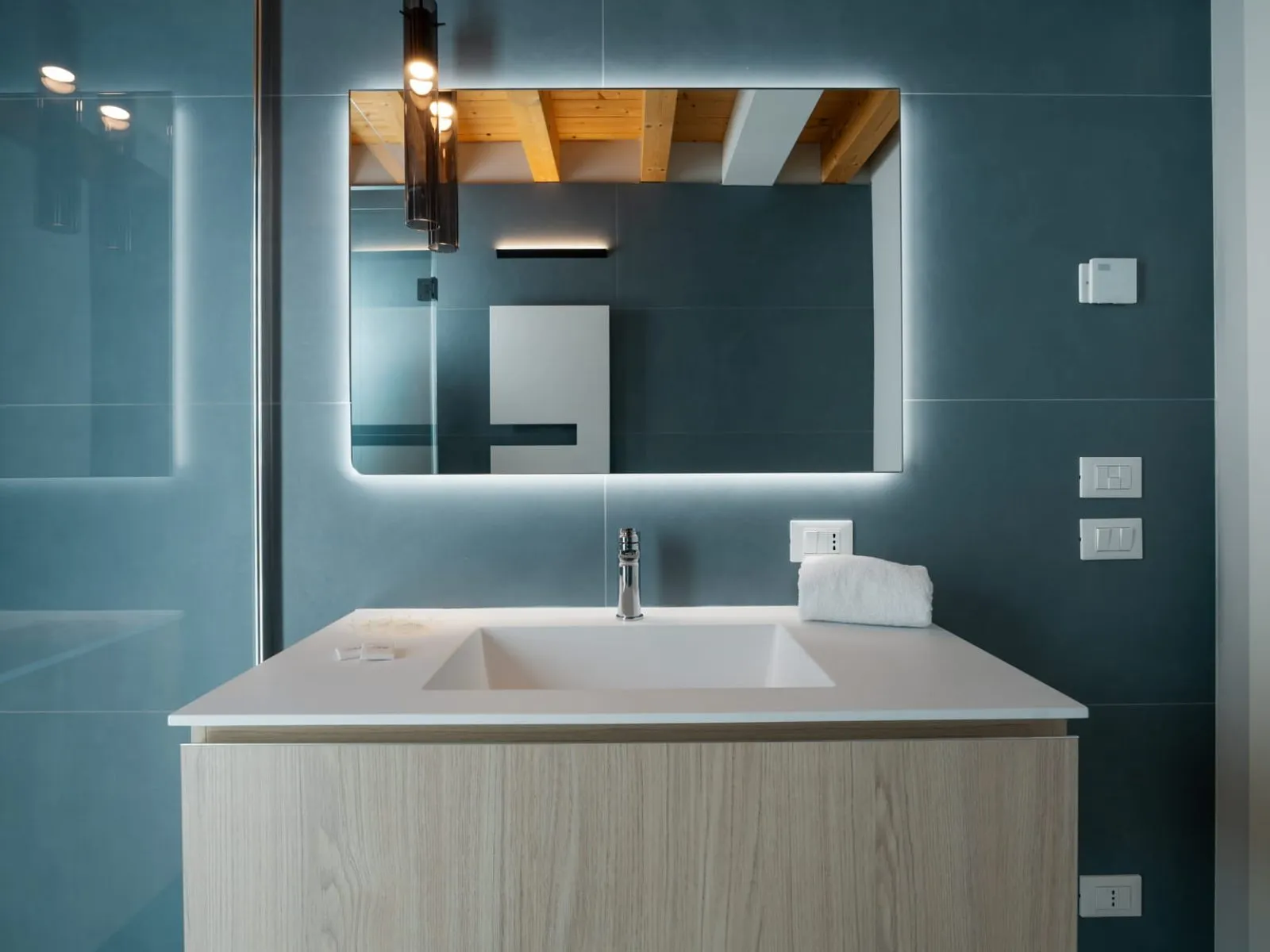 Dettaglio bagno con grande specchio retroilluminato e parete blu monolocale S-06 Ca' Toni Treviso