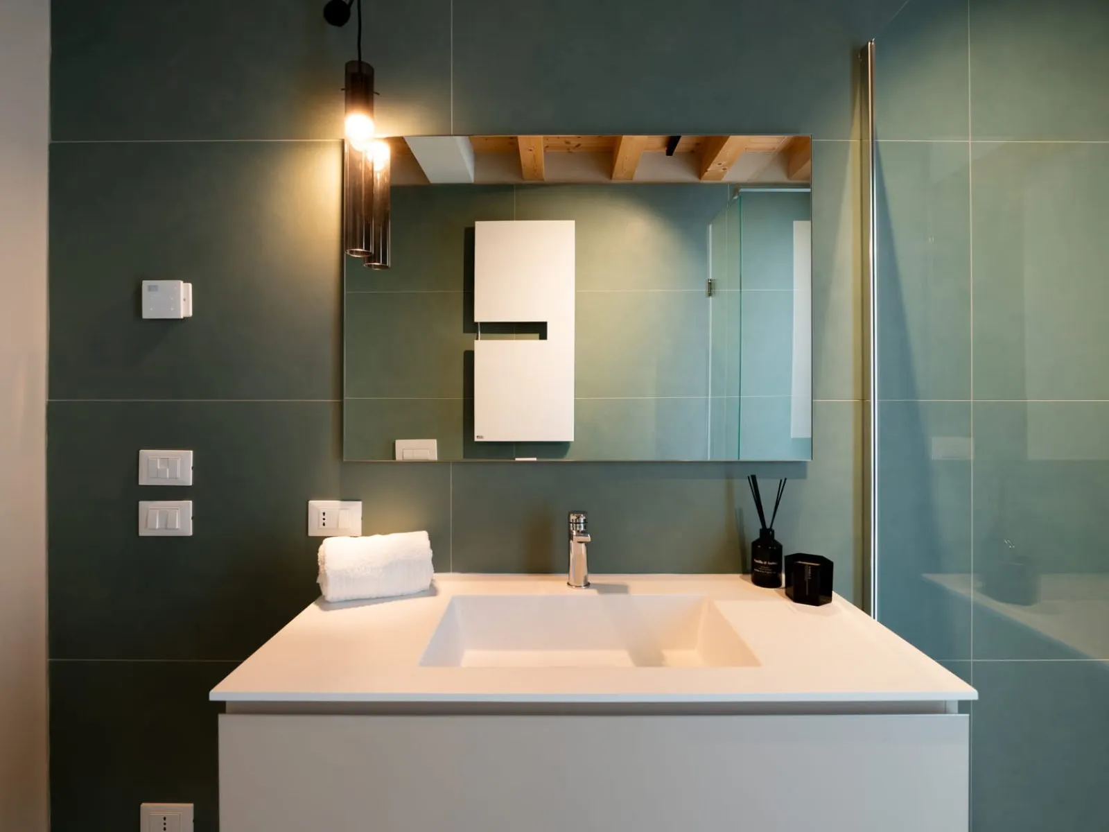 Dettaglio bagno con lavabo bianco e specchio su parete verde monolocale S-11 Ca' Toni Treviso