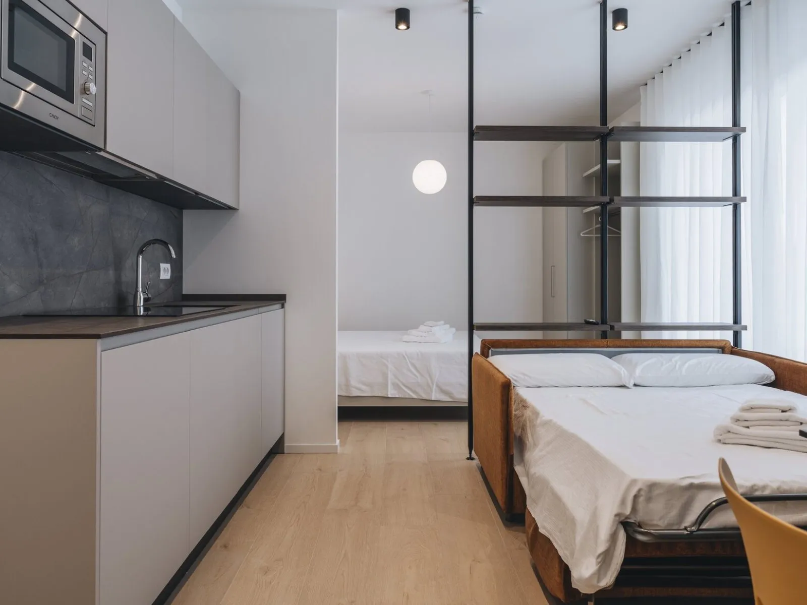 Divano letto aperto con letto matrimoniale sullo sfondo, tavolo pranzo e grande finestra – appartamento T-02 Ca' Sette Treviso