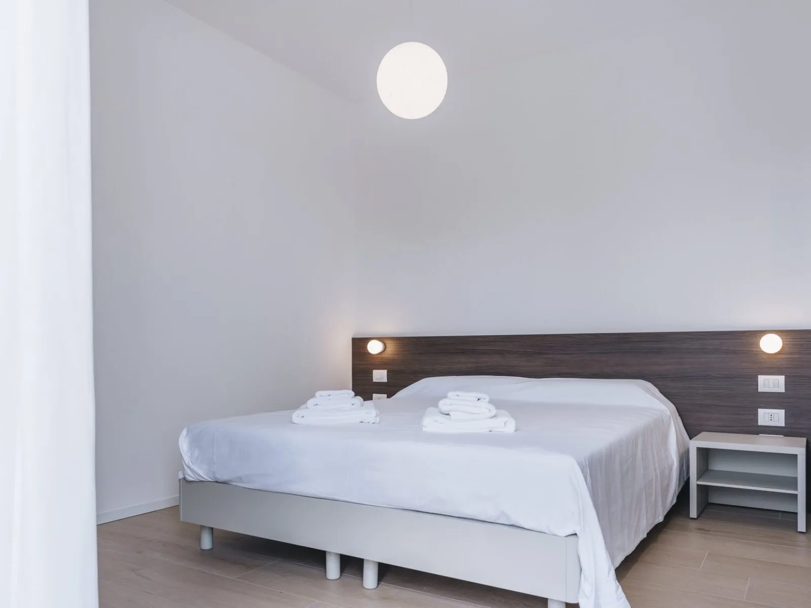 Letto matrimoniale con testiera in legno scuro, asciugamani e comodino bianco – appartamento T-03 Ca' Sette Treviso