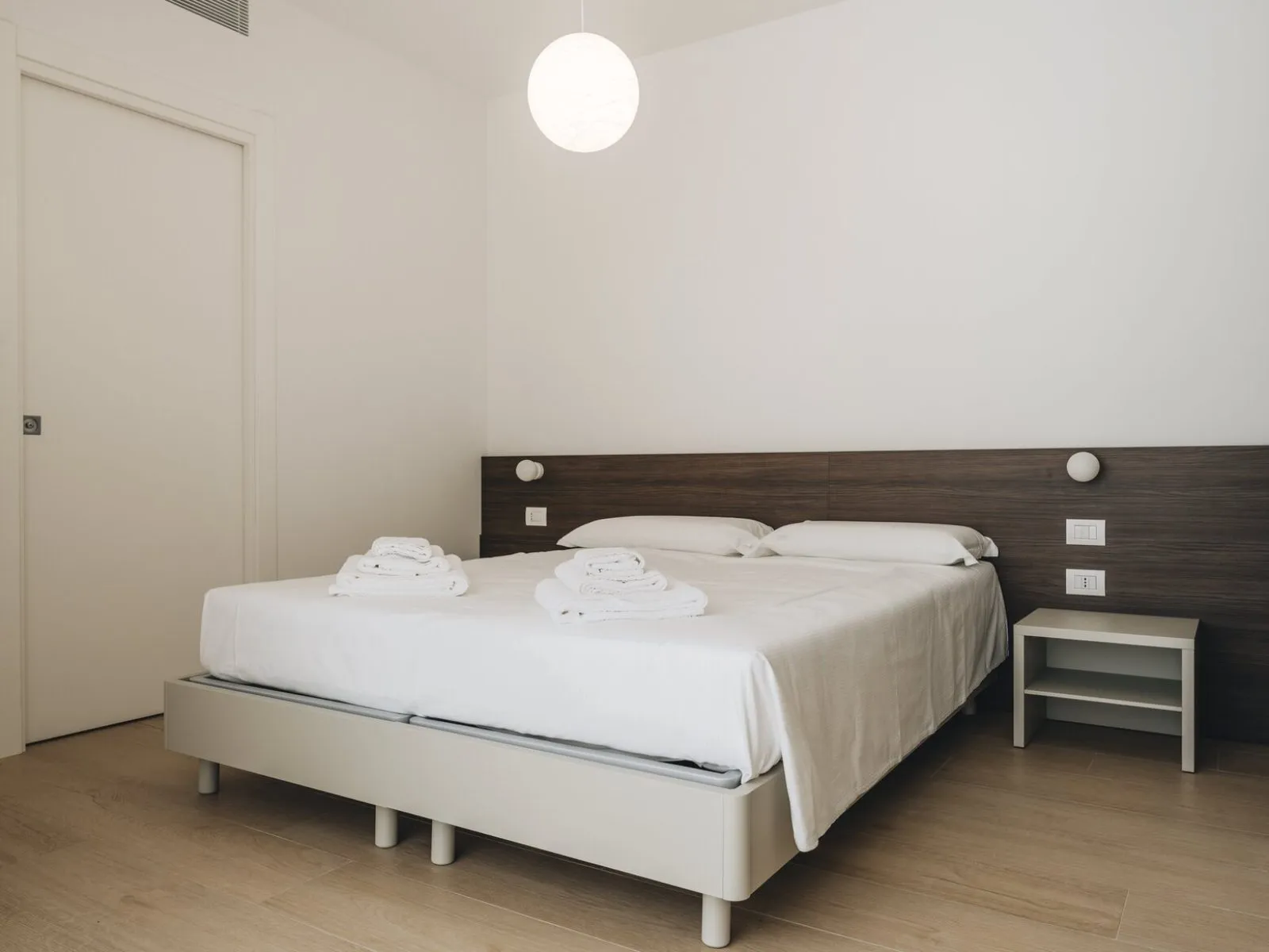 Double bed with dark wood headboard, fresh towels and white bedside table – apartment T-04 Ca' Sette Treviso