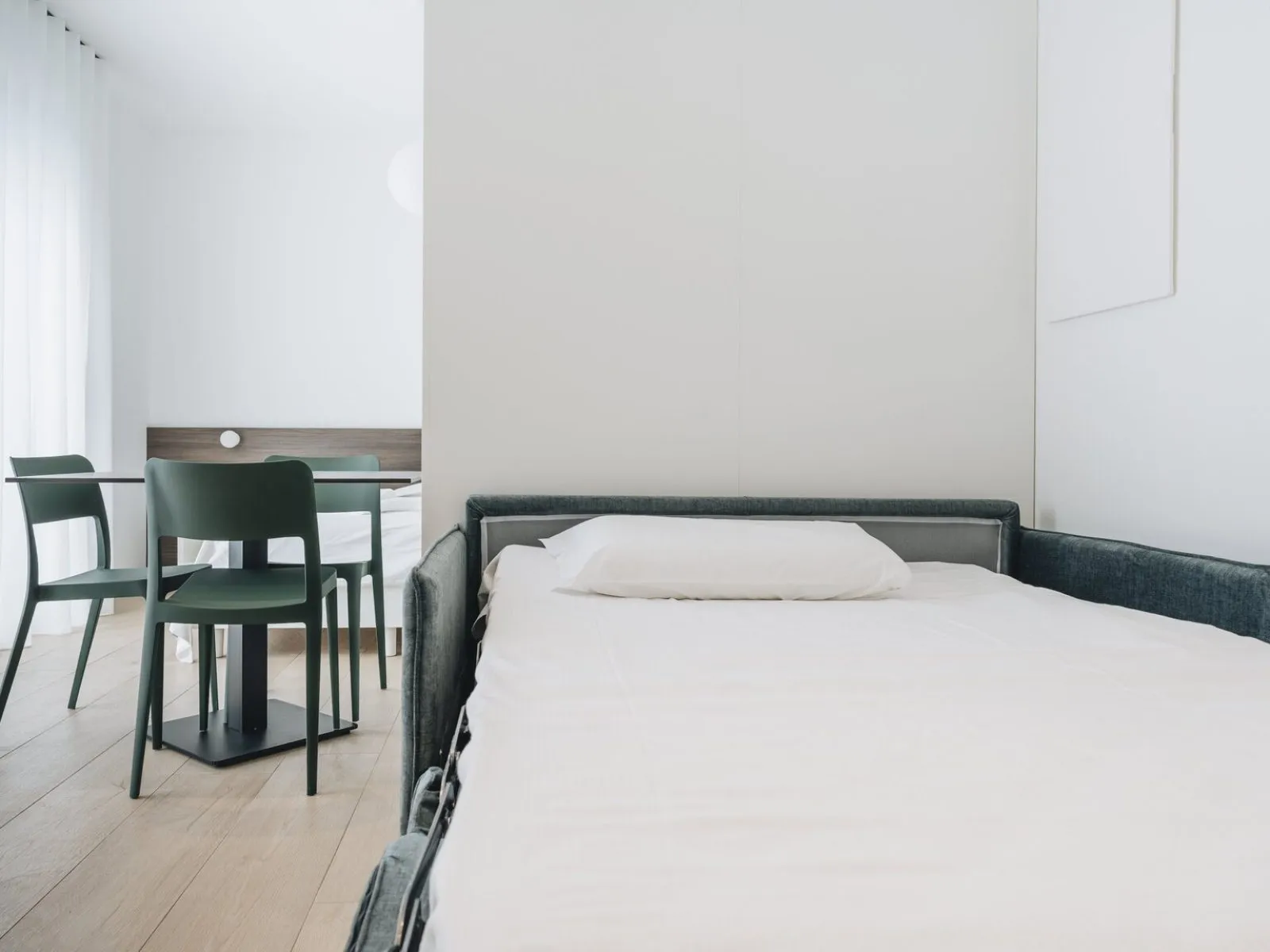 Sofa bed opened in the living area with round table and dark green chairs in the background – apartment T-06 Ca' Sette Treviso