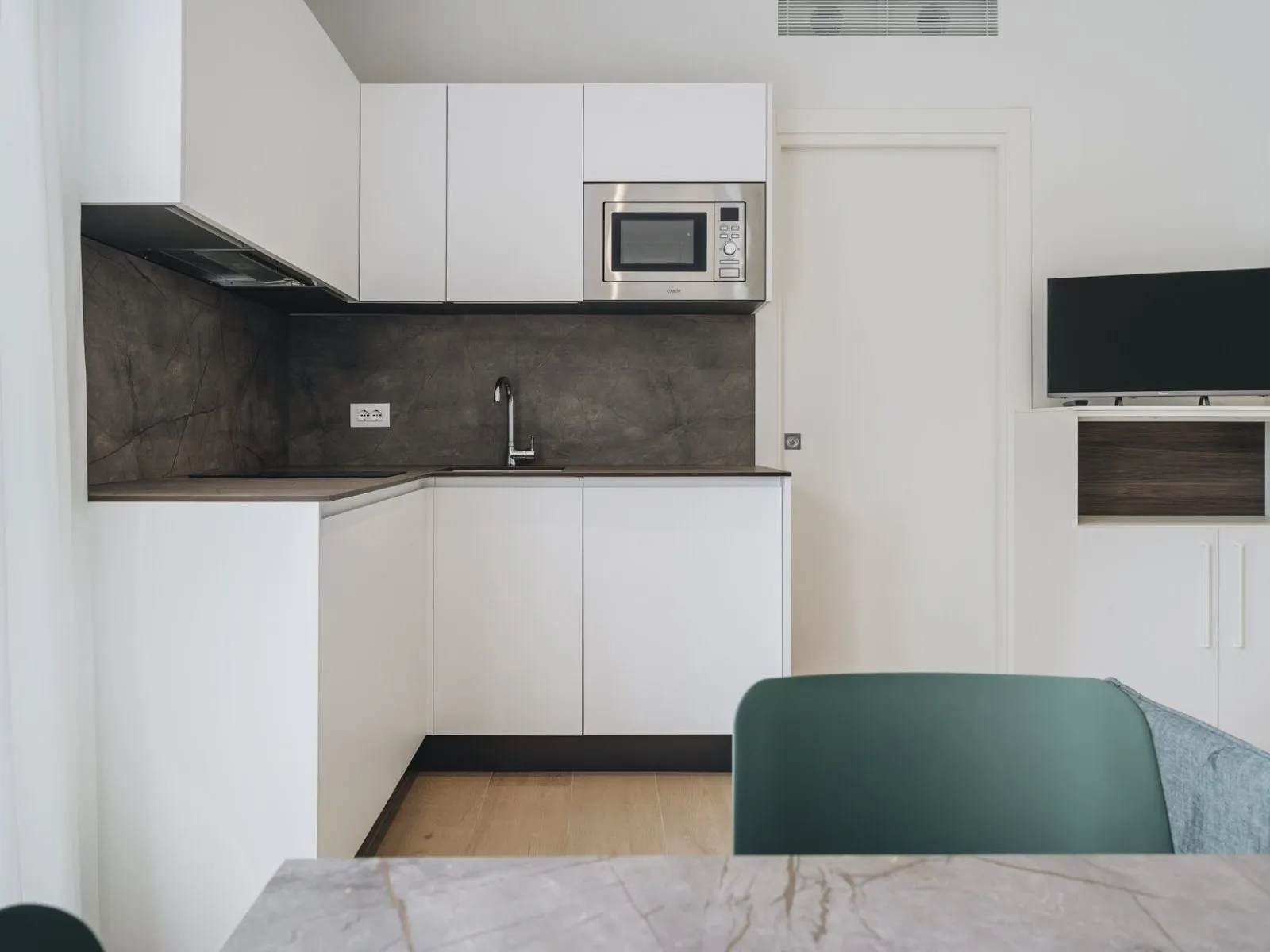 Cucina ad angolo attrezzata con pensili bianchi, microonde integrato e TV a parete – appartamento T-07 Ca' Sette Treviso