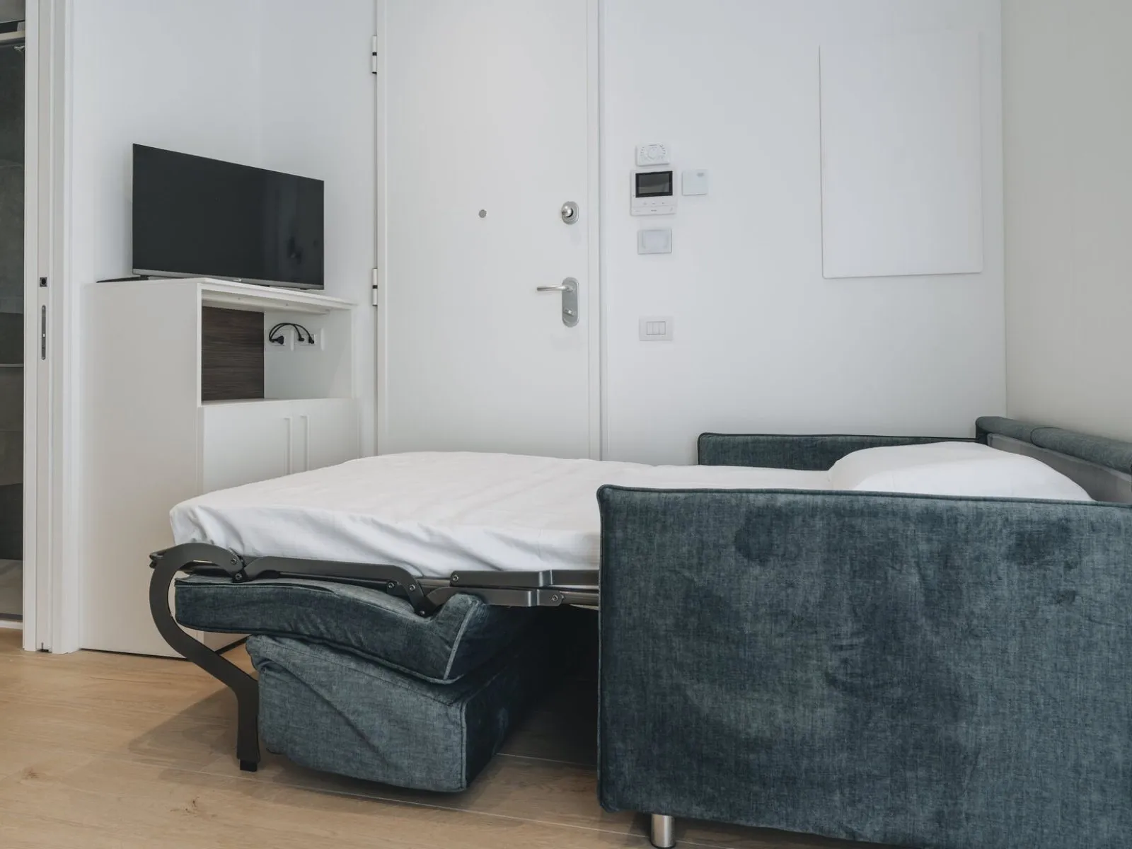 Divano letto aperto con TV, mobile contenitore e accesso al bagno con doccia – appartamento T-07 Ca' Sette Treviso